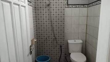Uma casa de banho pequena com sanita, chuveiro e um balde azul.