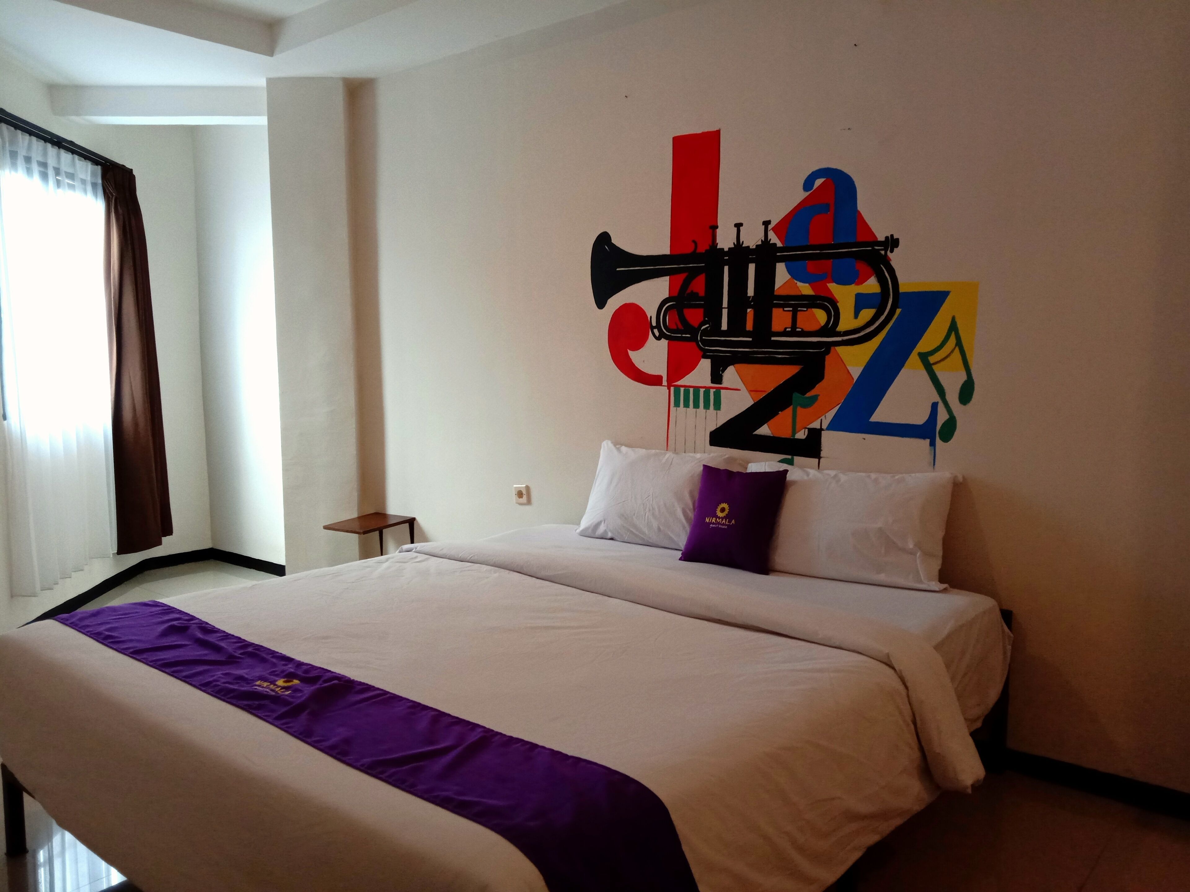 Une chambre d’hôtel avec un lit, une petite table et une fresque murale aux couleurs vives.