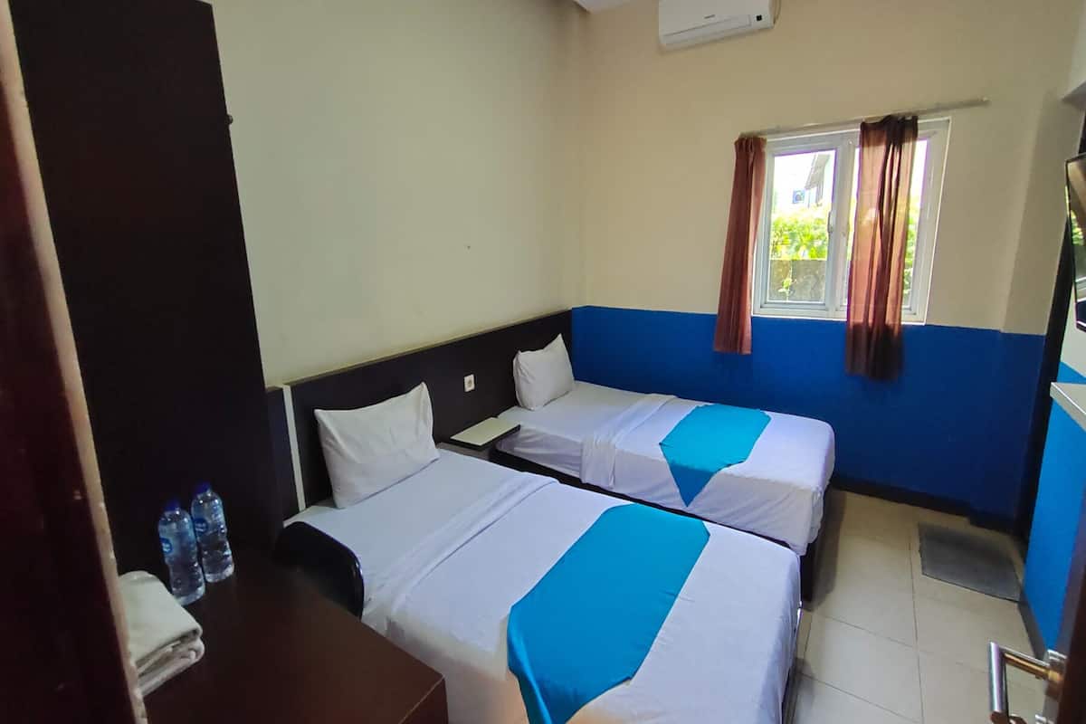 Habitación de hotel con dos camas, un escritorio, una silla, una ventana con cortinas y una botella de agua sobre el escritorio.