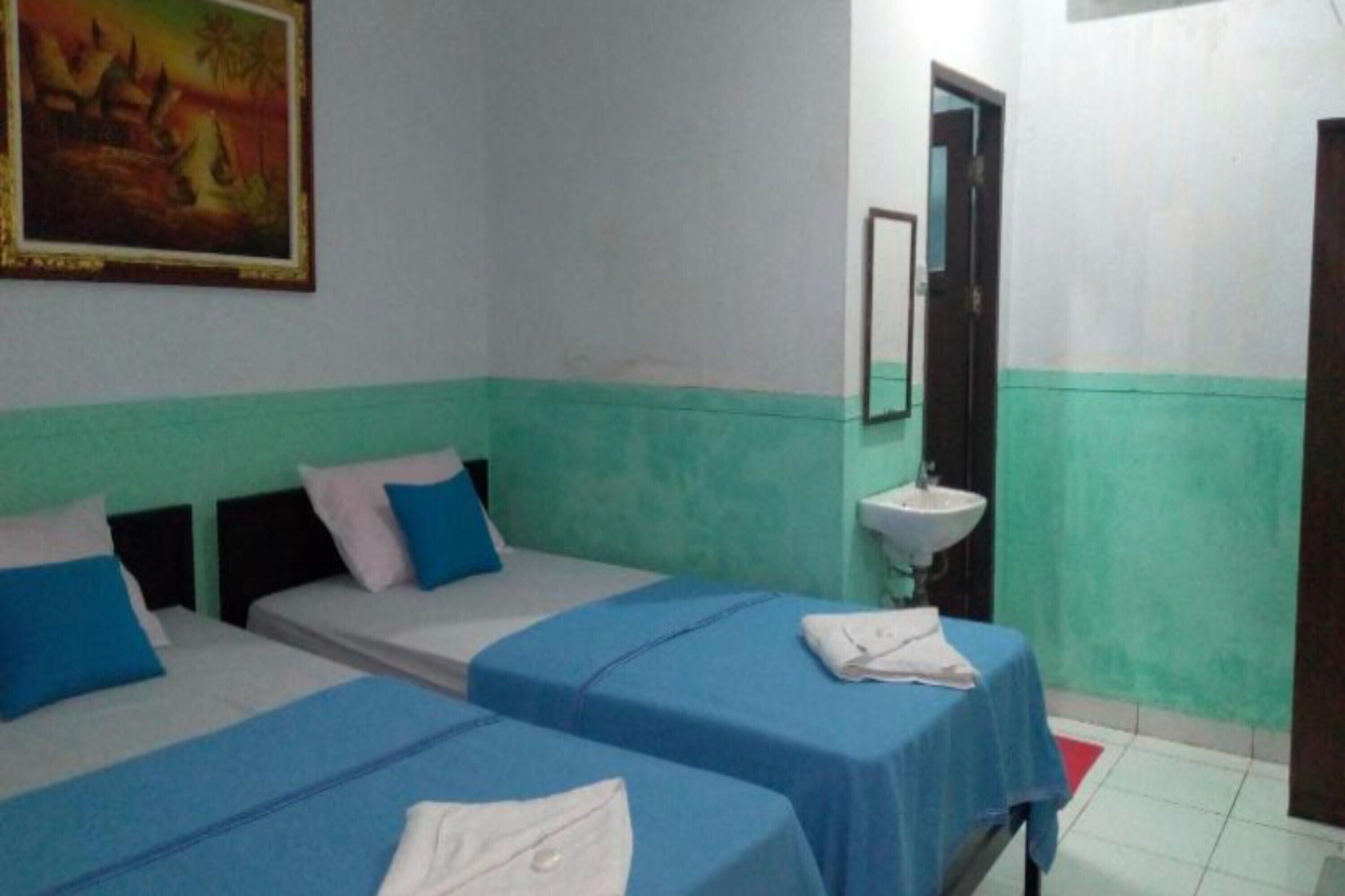 A hotel room with two beds, a sink, and a painting on the wall.