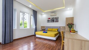 A bedroom with a wooden floor, a bed with a yellow bedspread, a wooden desk, and a window with curtains. - Phuc Villa (Da Nang)