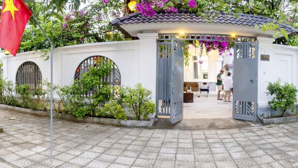 A traditional Vietnamese gate with a tiled roof, surrounded by lush greenery and purple flowers. - Phuc Villa (Da Nang)