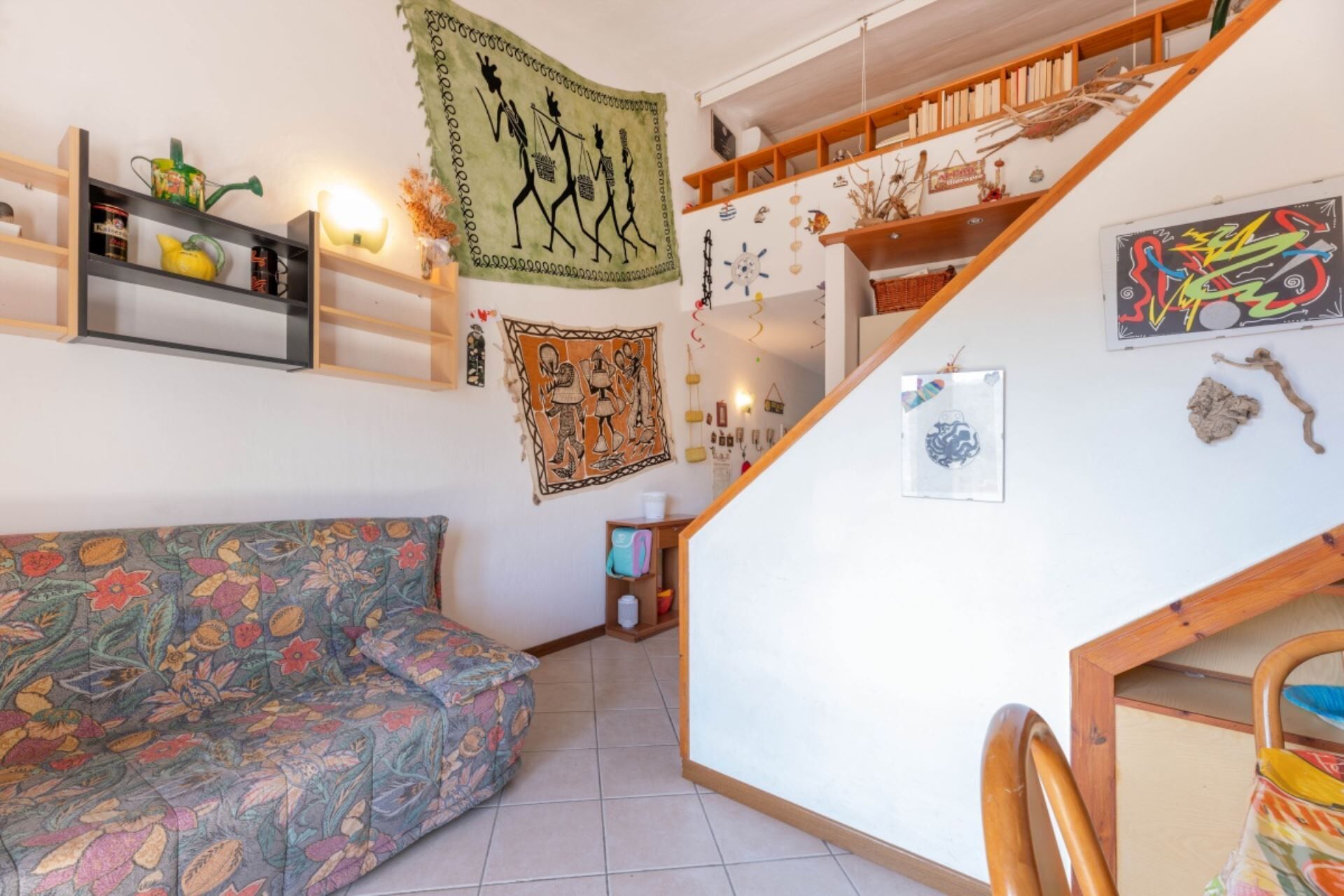 Una sala de estar acogedora con un sofá estampado, una escalera con estanterías y varios adornos en las paredes.