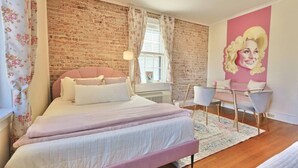 Une chambre avec un mur en briques, un lit avec une literie rose, un bureau avec une chaise et une décoration murale rose.