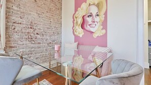 Un salon moderne avec une table basse en verre, un mur en briques et une grande fresque murale aux couleurs rose et blanche.