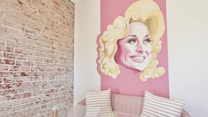 Une pièce avec un mur en briques, un mur rose orné d’un portrait et un canapé avec des coussins à rayures.