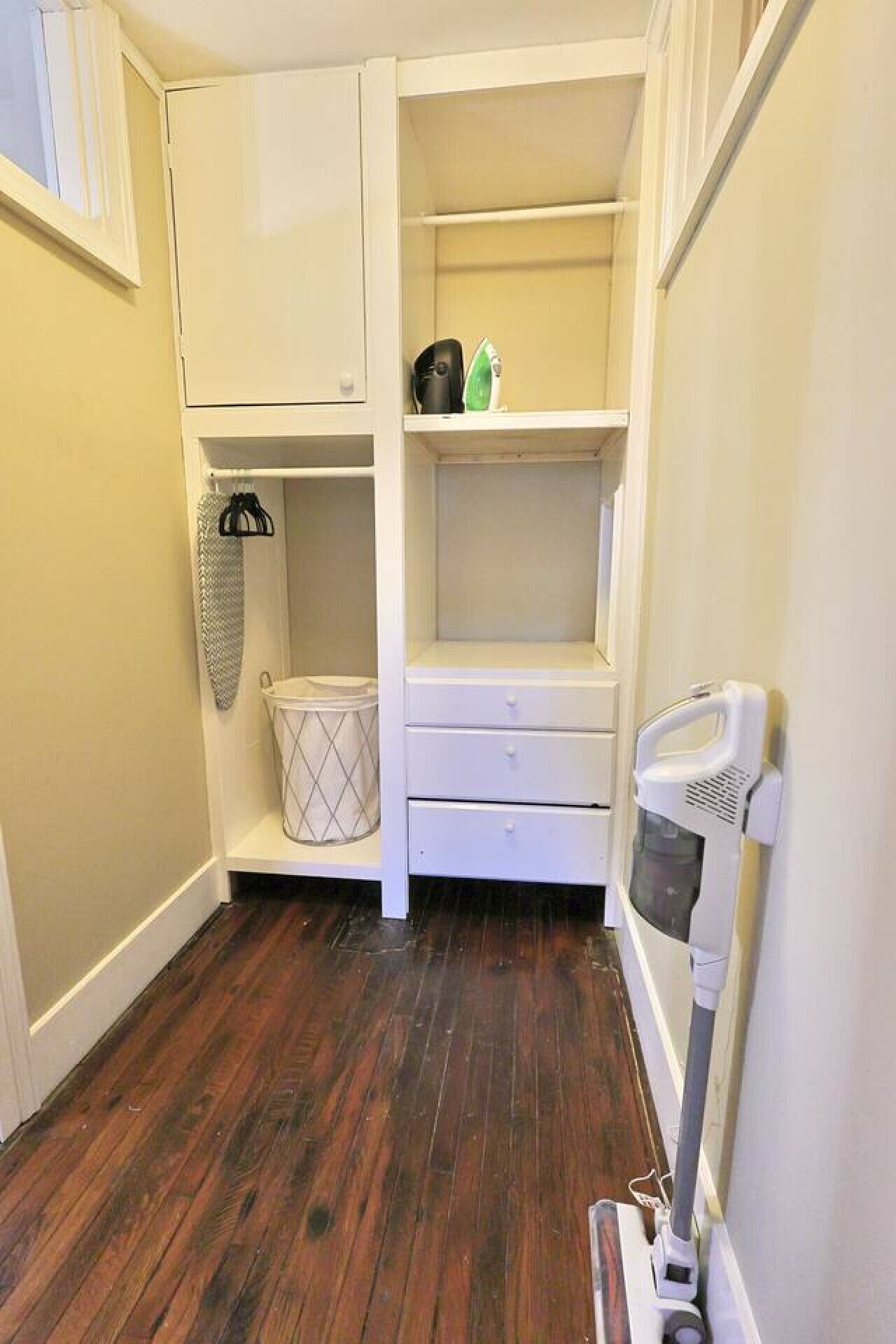 A small, compact kitchen with white cabinetry, a wooden floor, and basic appliances.