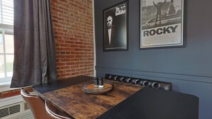 Un comedor con pared de ladrillo, una mesa de madera oscura, asientos tipo banca de cuero y carteles en la pared.