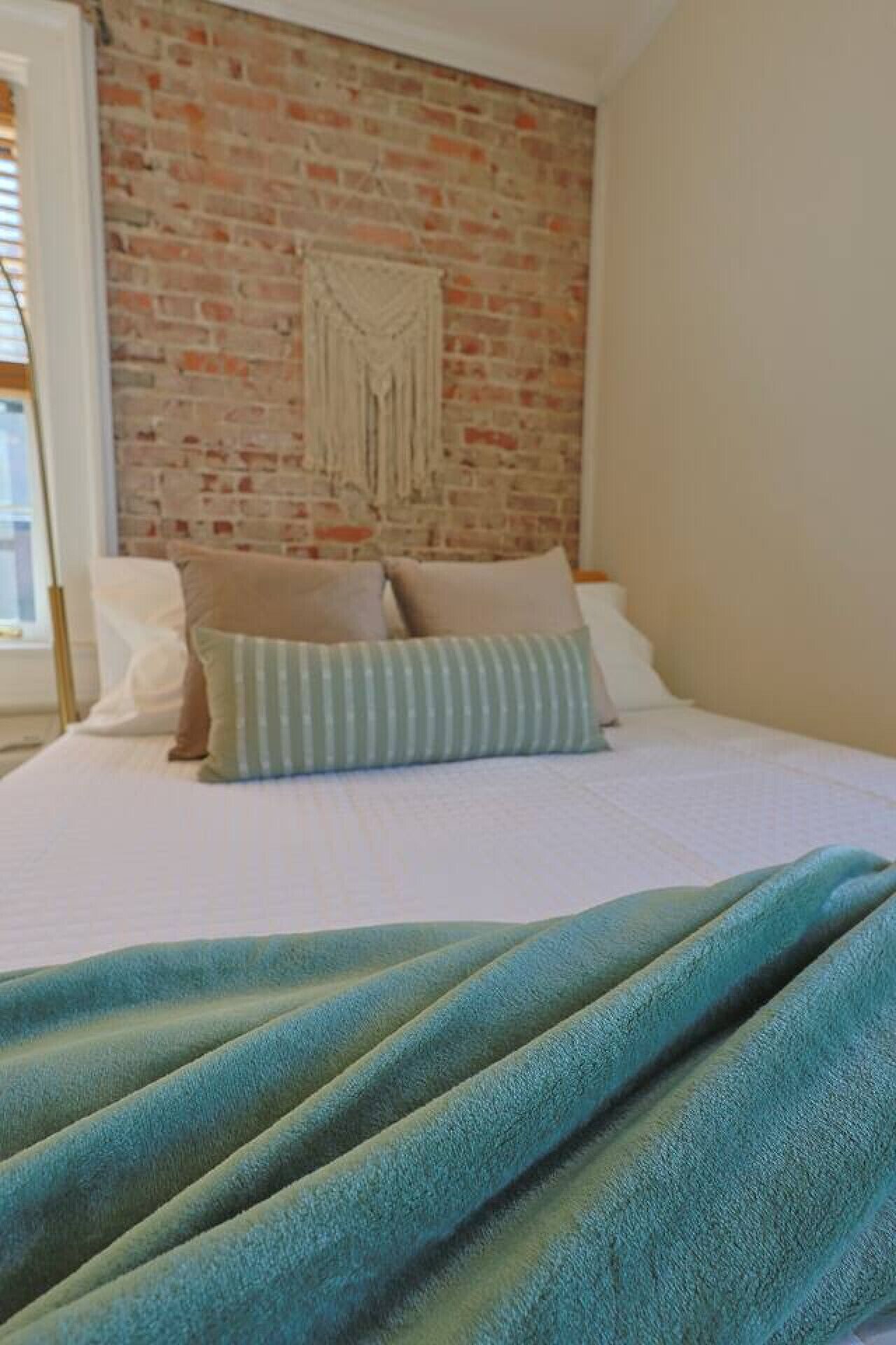 Ein Schlafzimmer mit Ziegelwand, einem Bett mit weißer Bettwäsche und einer senffarbenen Decke.