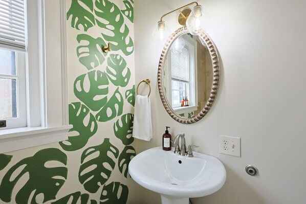 A bathroom with a white sink, a mirror with a decorative frame, and a window with blinds. - Boho Escape Studio - Walk to DT + Local Eateries (Knoxville)
