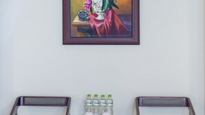 Una habitación con dos sillas de madera, una mesita con un jarrón de flores y un cuadro enmarcado en la pared.