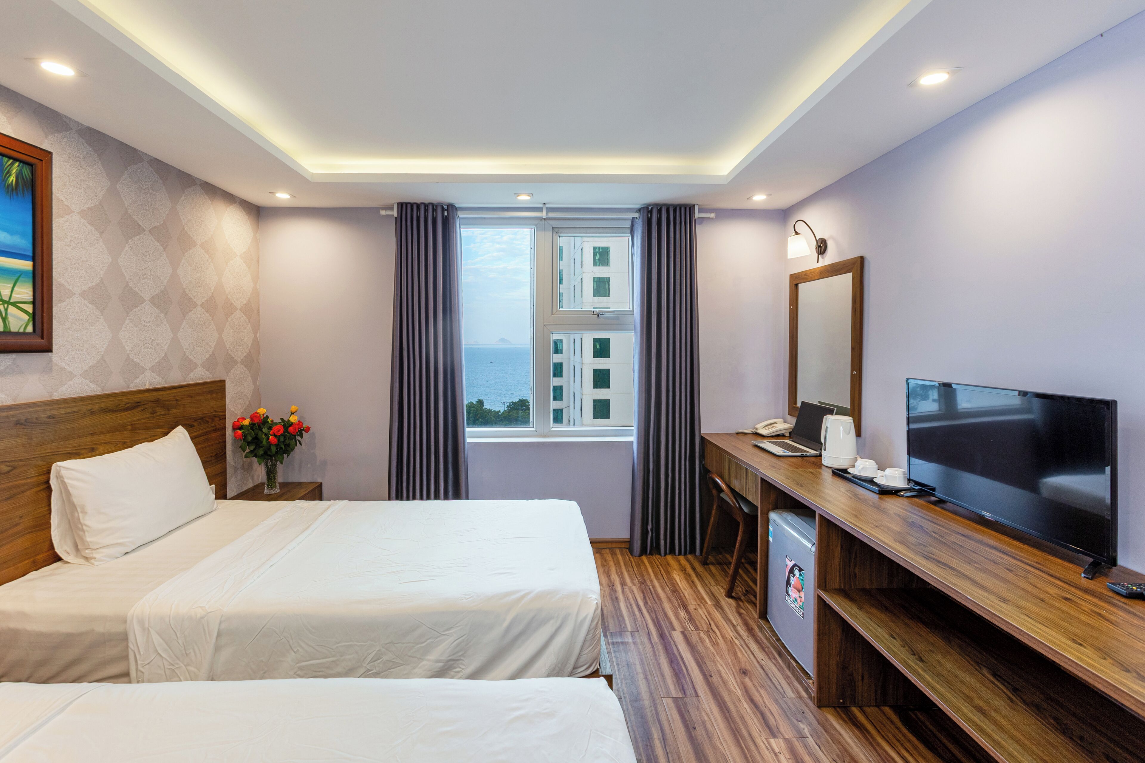 Quarto de hotel com duas camas, uma mesa de trabalho com televisão, cafeteira e vista para o mar.