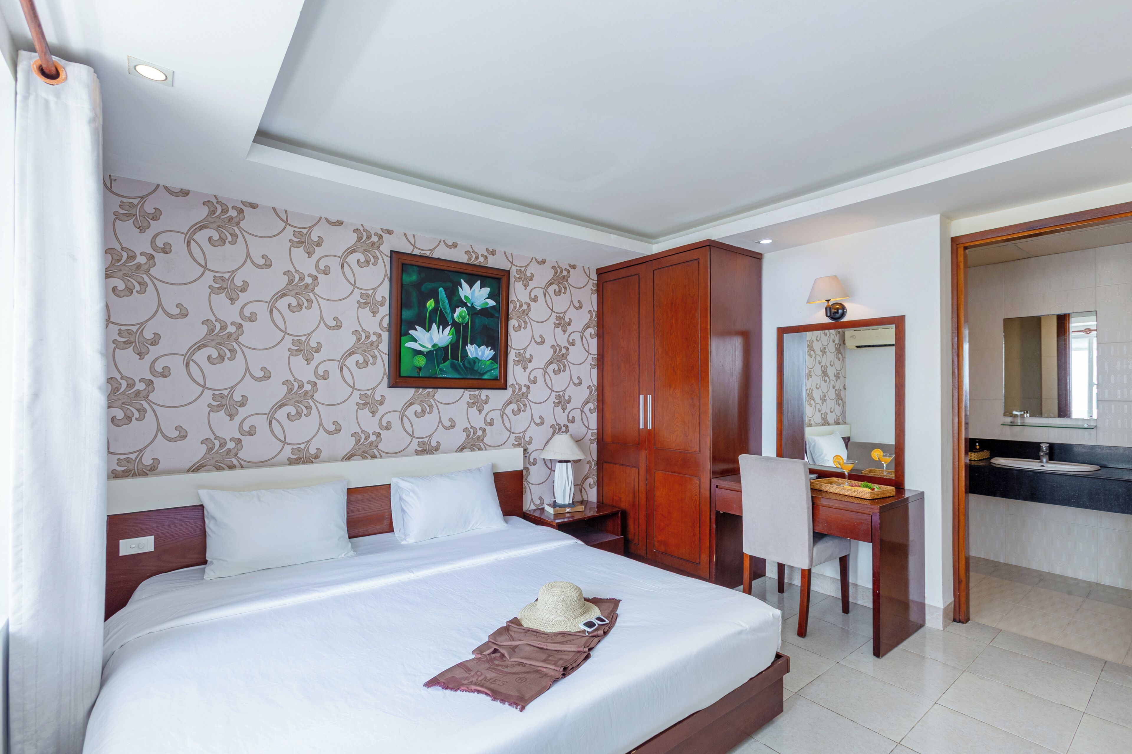A hotel room with a large bed, a desk, a wardrobe, and a bathroom visible through an open door.