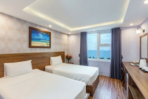 Une chambre d’hôtel avec deux lits, une tête de lit en bois, un tableau représentant une scène de plage, une fenêtre avec des rideaux et un bureau avec un téléphone et un ordinateur portable.