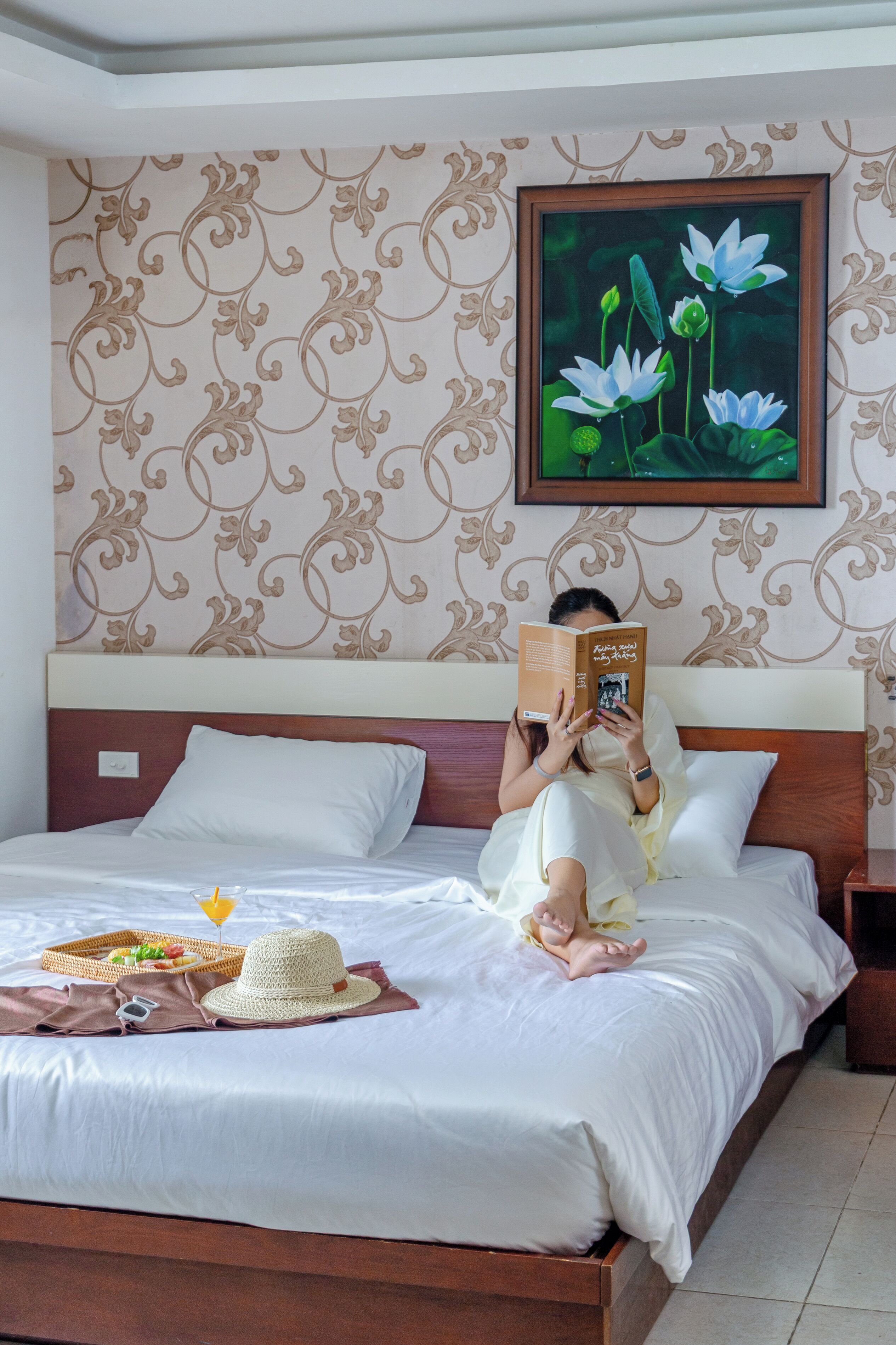 A bed with a wooden headboard, a tray with food, and a framed picture of flowers on the wall.