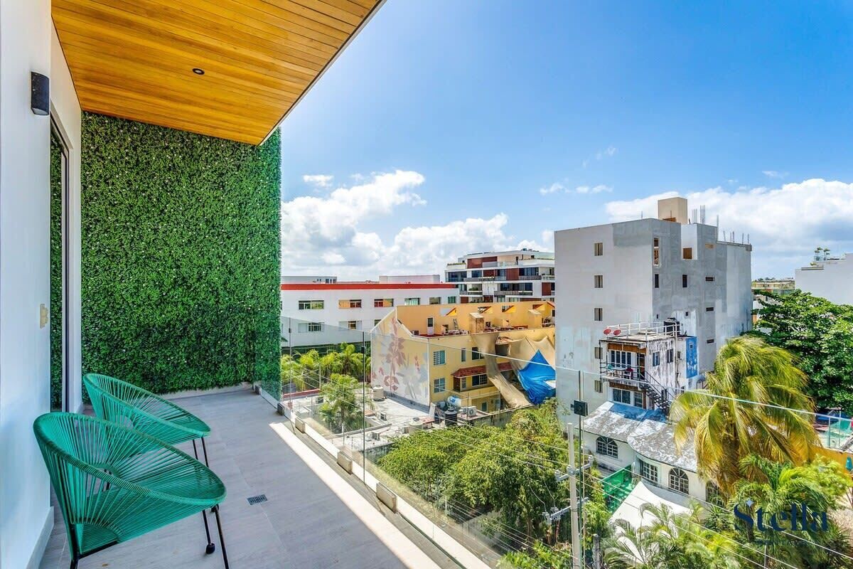 Un balcon avec des chaises vertes, un plafond en bois et une vue sur des immeubles et la verdure.