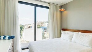 A hotel room with a large bed, a desk, and a view of the city through the window. - Downtown Condo, Rooftop Pool, Steps to 5th (Playa del Carmen)