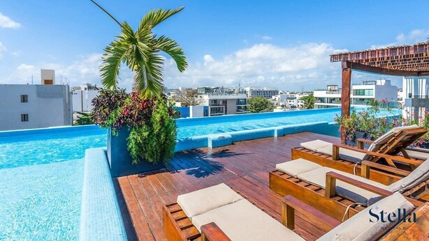 A rooftop pool area with a wooden deck, lounge chairs, and a view of the cityscape. - Downtown Condo, Rooftop Pool, Steps to 5th (Playa del Carmen)