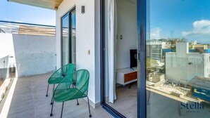A balcony with a glass door, a green chair, and a TV on a stand. - Downtown Condo, Rooftop Pool, Steps to 5th (Playa del Carmen)