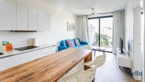 A modern kitchen with white cabinets, a wooden dining table, and a blue sofa with colorful cushions. - Downtown Condo, Rooftop Pool, Steps to 5th (Playa del Carmen)