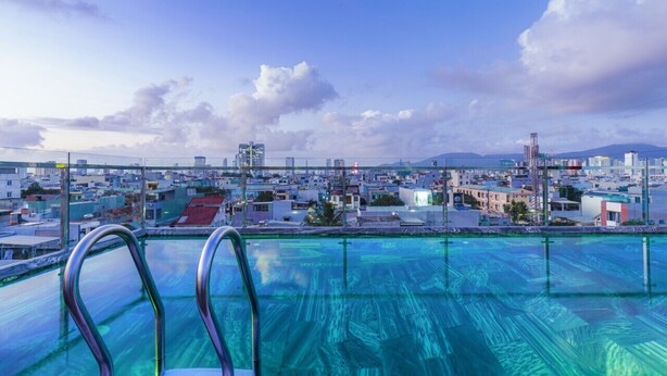 Une piscine sur le toit, avec une eau d’un bleu cristallin, entourée d’un paysage urbain composé d’immeubles et, au loin, d’une chaîne de montagnes.