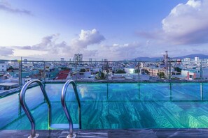 A rooftop pool with clear blue water, surrounded by a cityscape with buildings and a distant mountain range. - M.IA BEACH HOTEL & APARTMENT DA NANG (Da Nang)