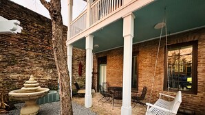 A courtyard with a brick wall, a tree, a stone fountain, outdoor seating, and a hanging swing. - Downtown Mobile near Dauphin, St Louis, Greer's, Saenger, Restaurants - Unit A (Mobile)