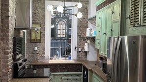 A kitchen with a brick wall, a stainless steel stove, green cabinets, and a large window with a stained glass design. - Downtown Mobile near Dauphin, St Louis, Greer's, Saenger, Restaurants - Unit A (Mobile)