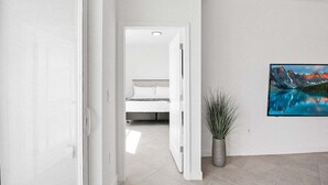 A hallway leading to a bedroom with a bed, a potted plant, and a painting on the wall. - Lakefront villa -  pet friendly - near beaches - Hibiscus Haven (Englewood)