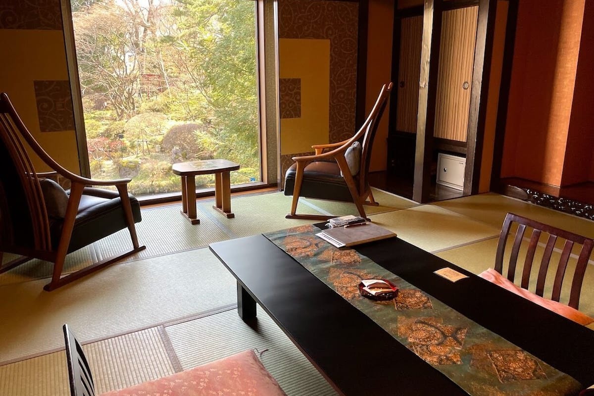 Ett traditionellt japanskt rum med tatamimattor på golvet, ett lågt bord och trästolar.
