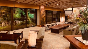 Un espace intérieur spacieux avec une grande table en bois, plusieurs chaises et un canapé. Une grande fenêtre offre une vue sur un jardin.