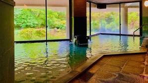 Une piscine intérieure aux parois en verre transparent, dotée d’un sol en pierre et offrant une vue sur un jardin luxuriant.