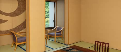 Una habitación tradicional japonesa con suelo de tatami, una mesa baja con mantel estampado y dos sillas de madera.