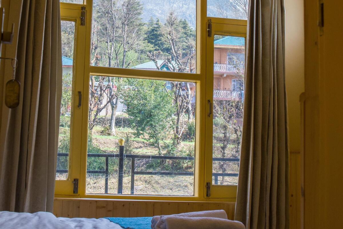 Une chambre avec un lit, une fenêtre avec des rideaux et une vue sur une montagne et des arbres.
