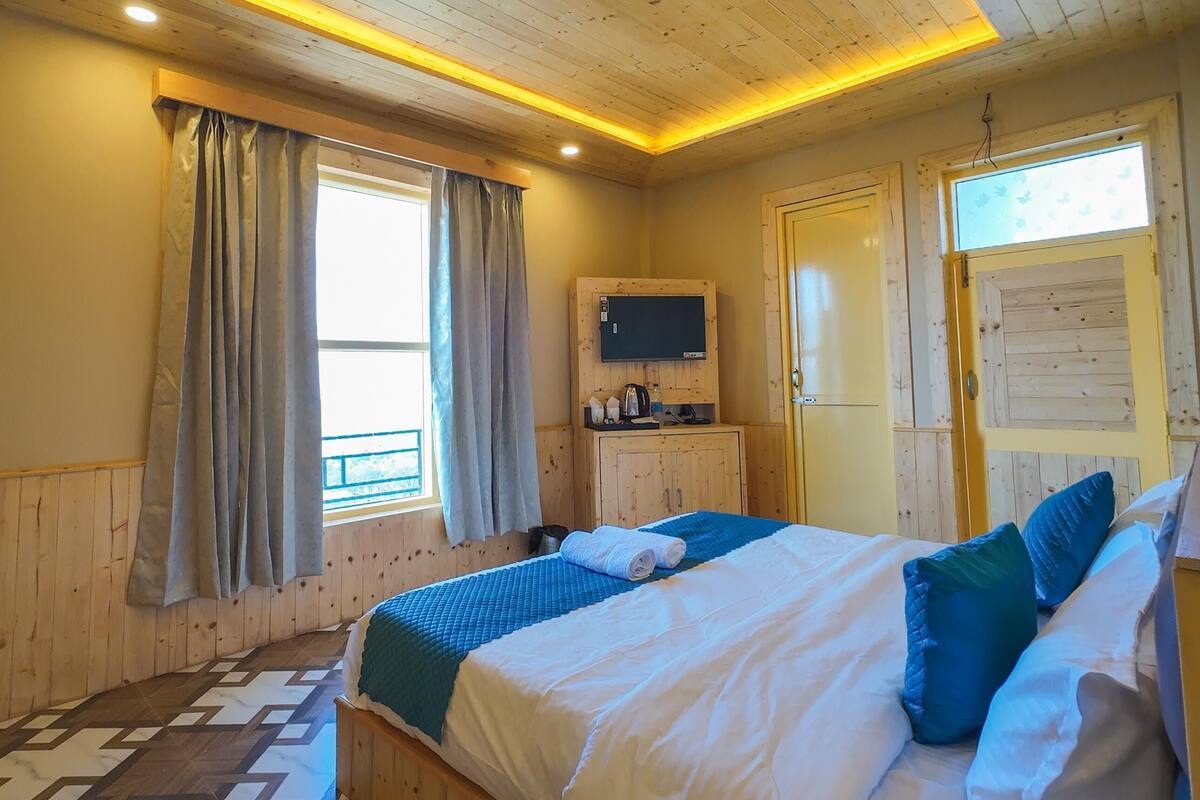 Une chambre à coucher aux murs lambrissés, avec un lit, des rideaux, un téléviseur et une fenêtre.