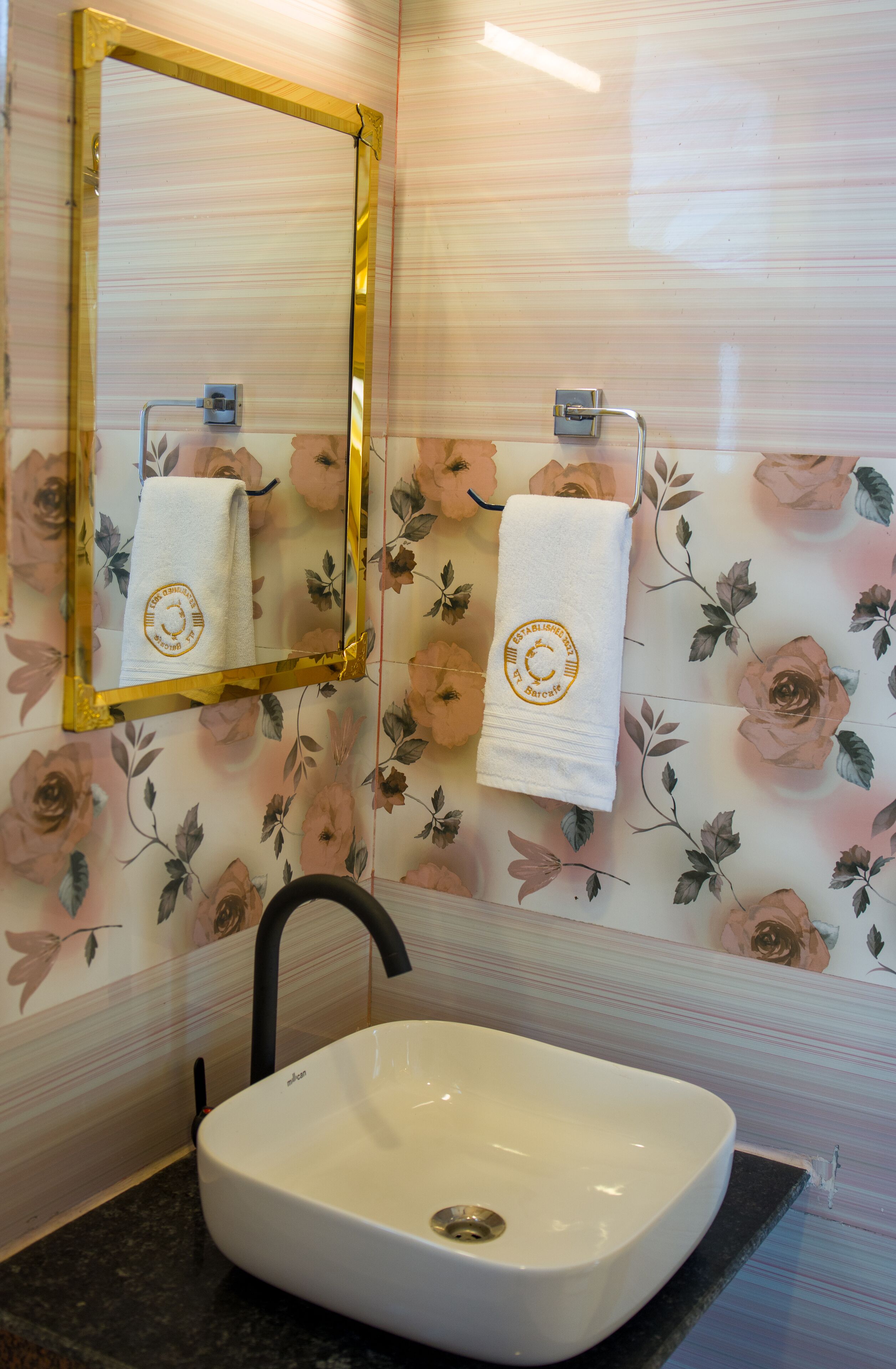 A bathroom with a white sink, a mirror with a gold frame, and floral wallpaper.