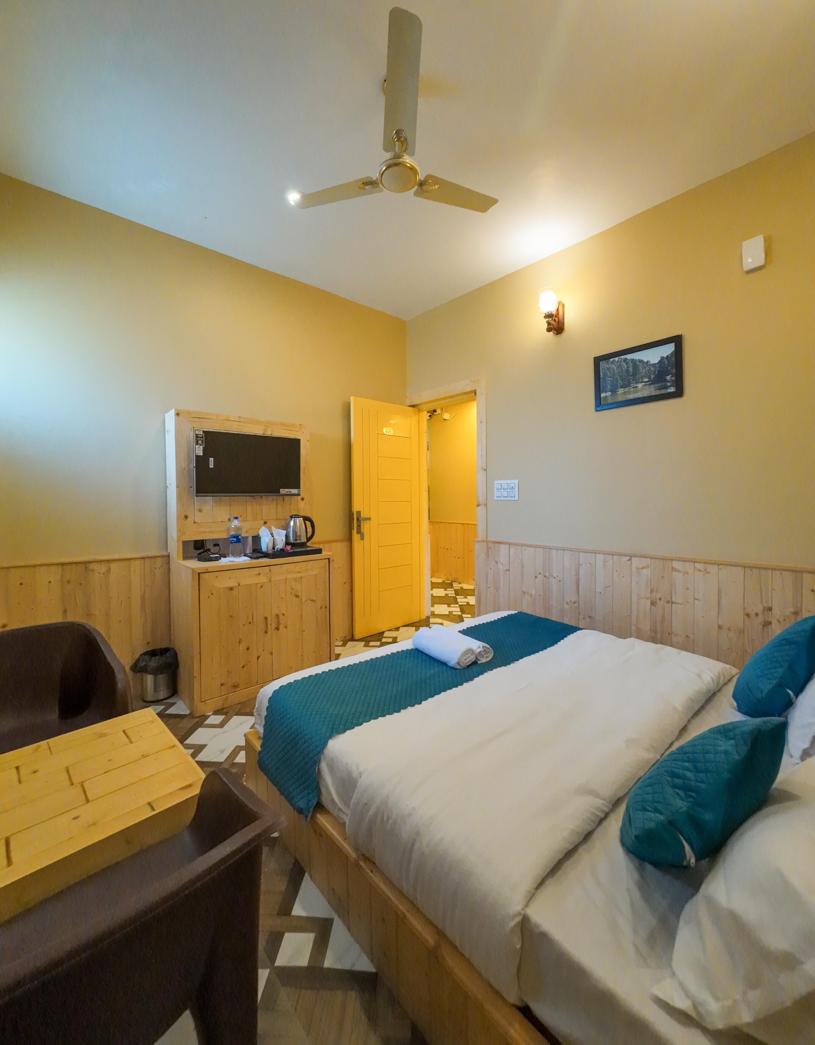 A hotel room with a bed, a desk, a chair, a television, and a door leading to another room.