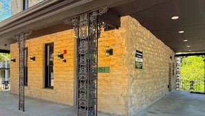 Un edificio de piedra con un porche cubierto, un cartel con número y un área vallada.