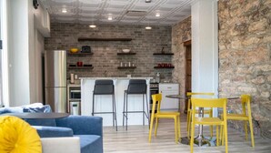 Una sala de estar moderna con un sofá azul, sillas amarillas y un comedor con pared de piedra y salpicadero de ladrillo.