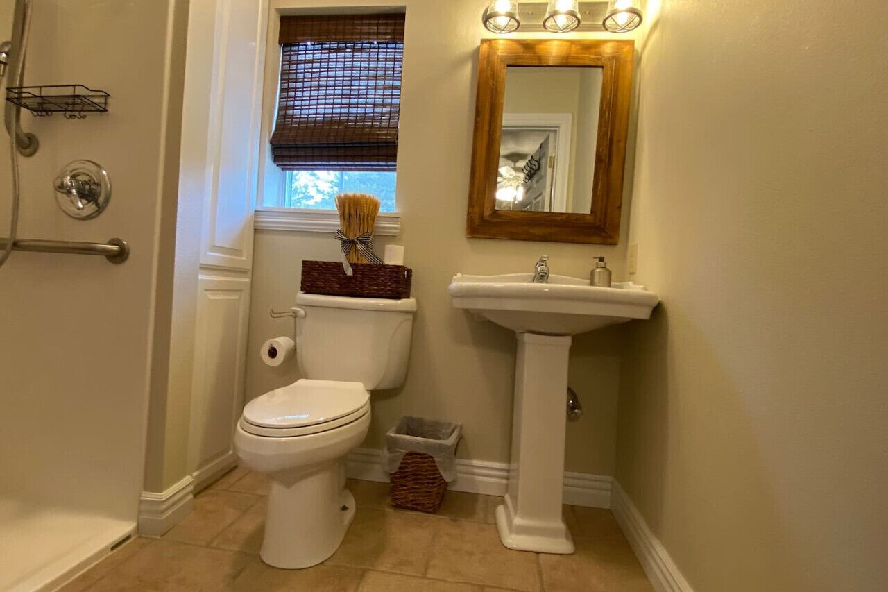 Et badeværelse med toilet, håndvask og et vindue med persienner.