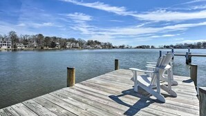 A wooden pier with two Adirondack chairs facing a calm lake, surrounded by residential buildings under a clear sky. - Waterfront Home with Private Dock, Community Beach (Annapolis)
