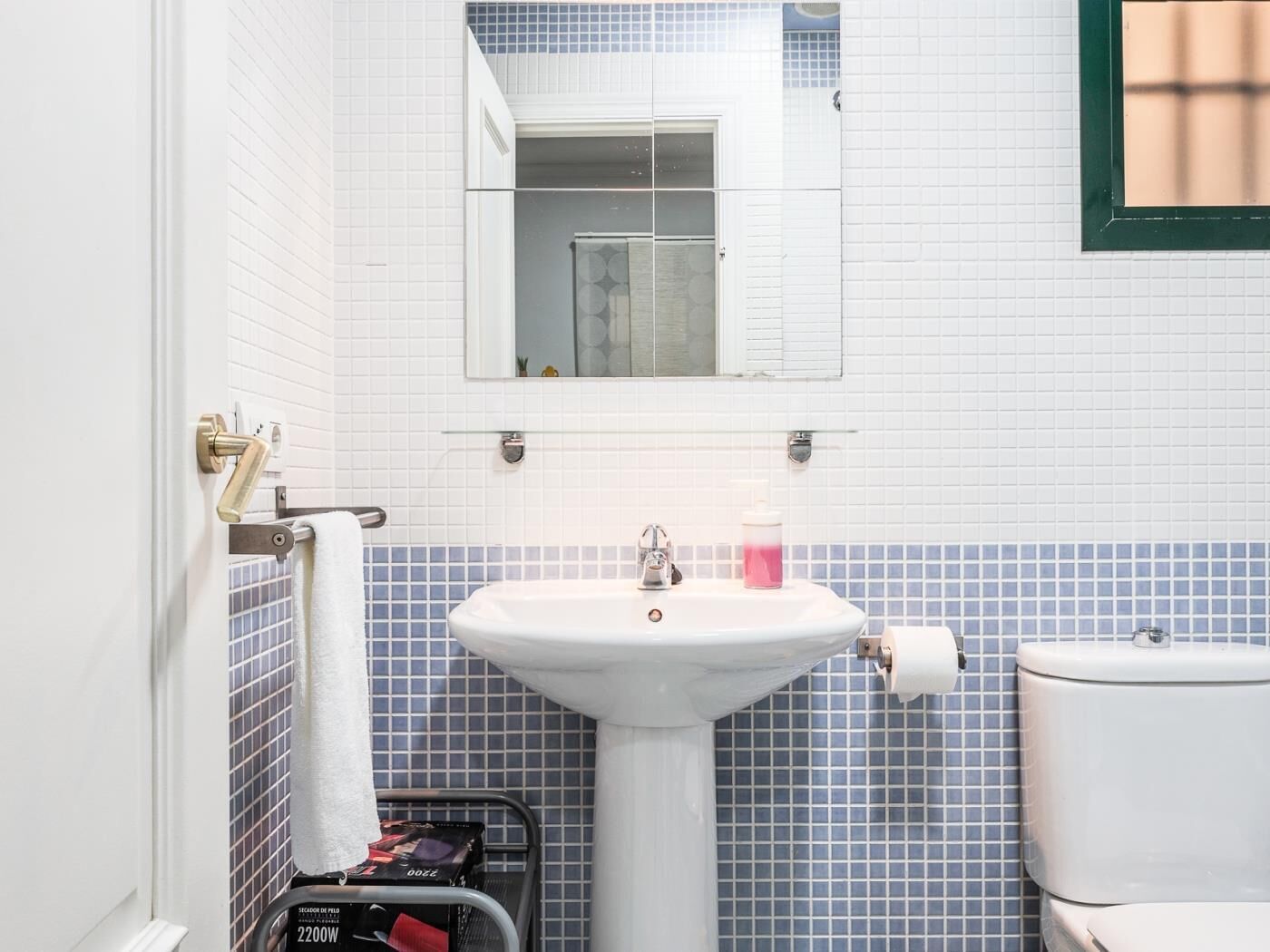 Une salle de bain avec un lavabo blanc, un miroir et des toilettes. On y trouve un porte-serviettes sur lequel est accrochée une serviette blanche.