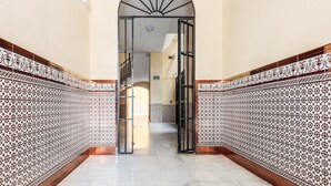 Um corredor com paredes de azulejos estampados e chão de mármore, que leva a uma escadaria.