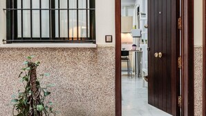 Uma porta dá acesso a um quarto com chão de azulejos, uma janela com grades e uma planta ao lado da porta.