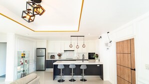 A modern kitchen with a central island, bar stools, a refrigerator, and a wooden door. - The Scoop Sea view Kamala 10km to Patong (Kamala)