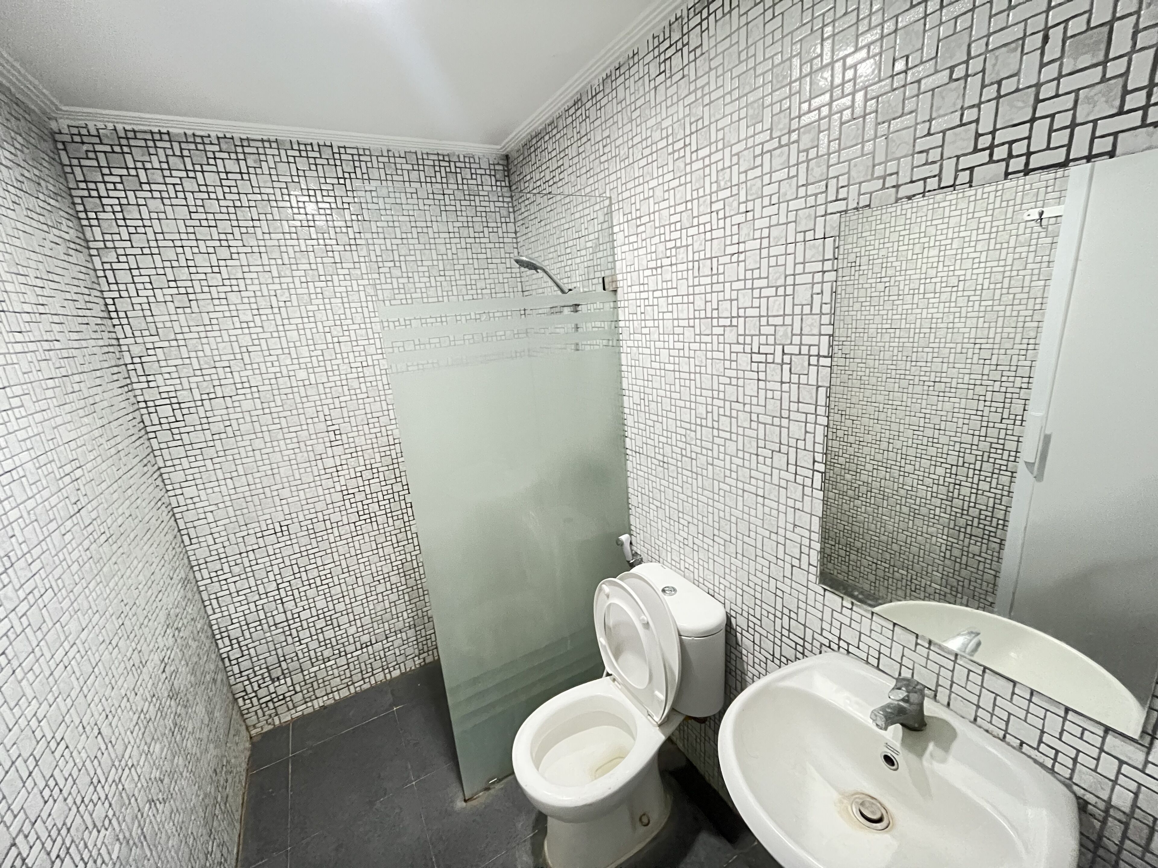 A bathroom with a tiled floor, a toilet, a sink, and a shower area.