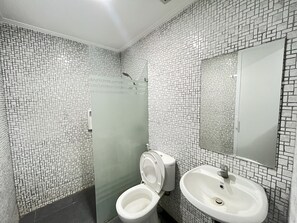 A bathroom with a tiled wall, a toilet, a sink, and a shower. - OYO 93721 RuPA Near LRT Velodrome 2 Rawamangun (Jakarta)