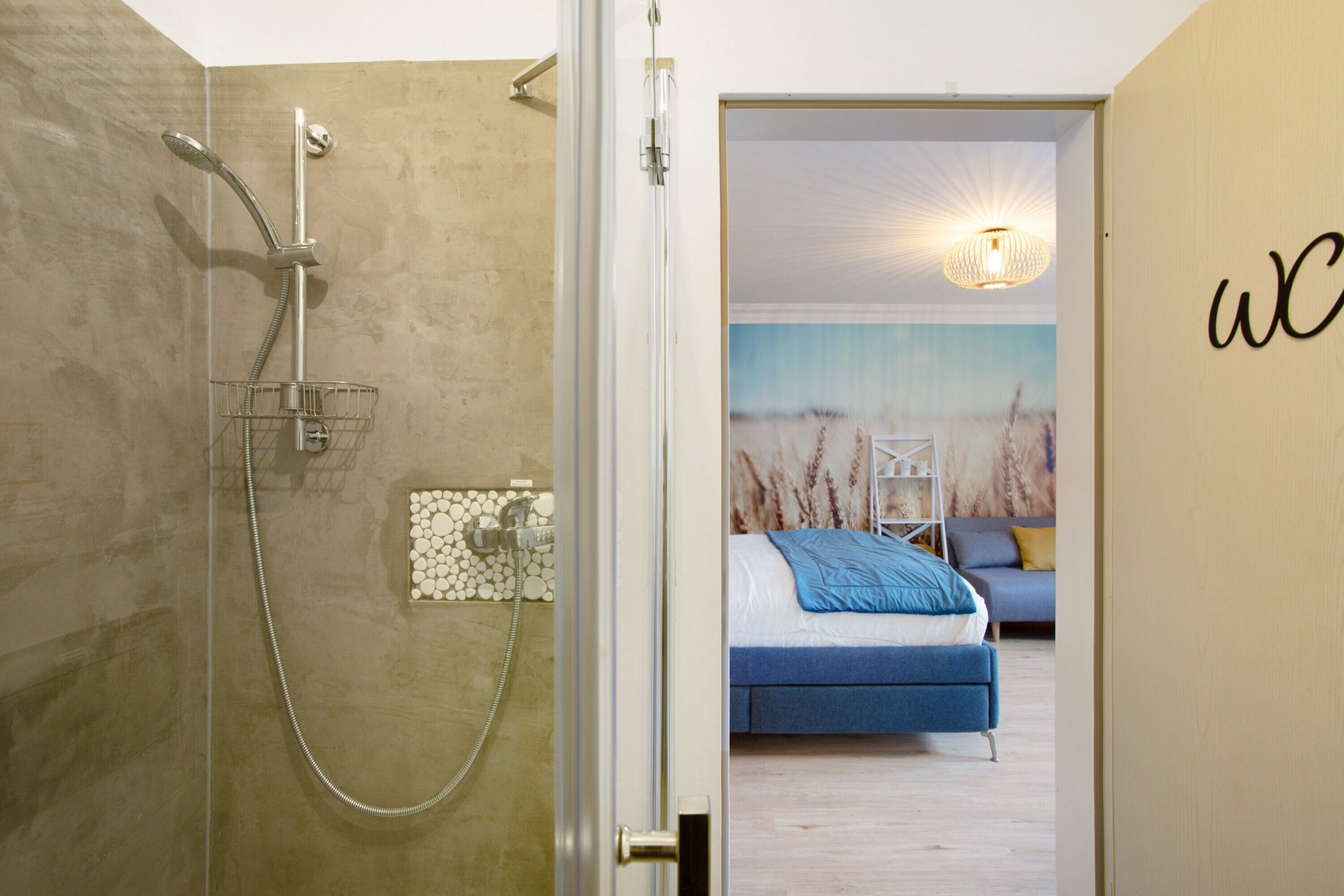 A modern bathroom with a glass shower enclosure, a visible towel rack, and a wall-mounted light fixture.