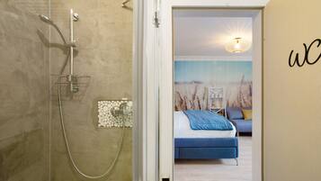 A modern bathroom with a glass shower enclosure, a visible towel rack, and a wall-mounted light fixture.
