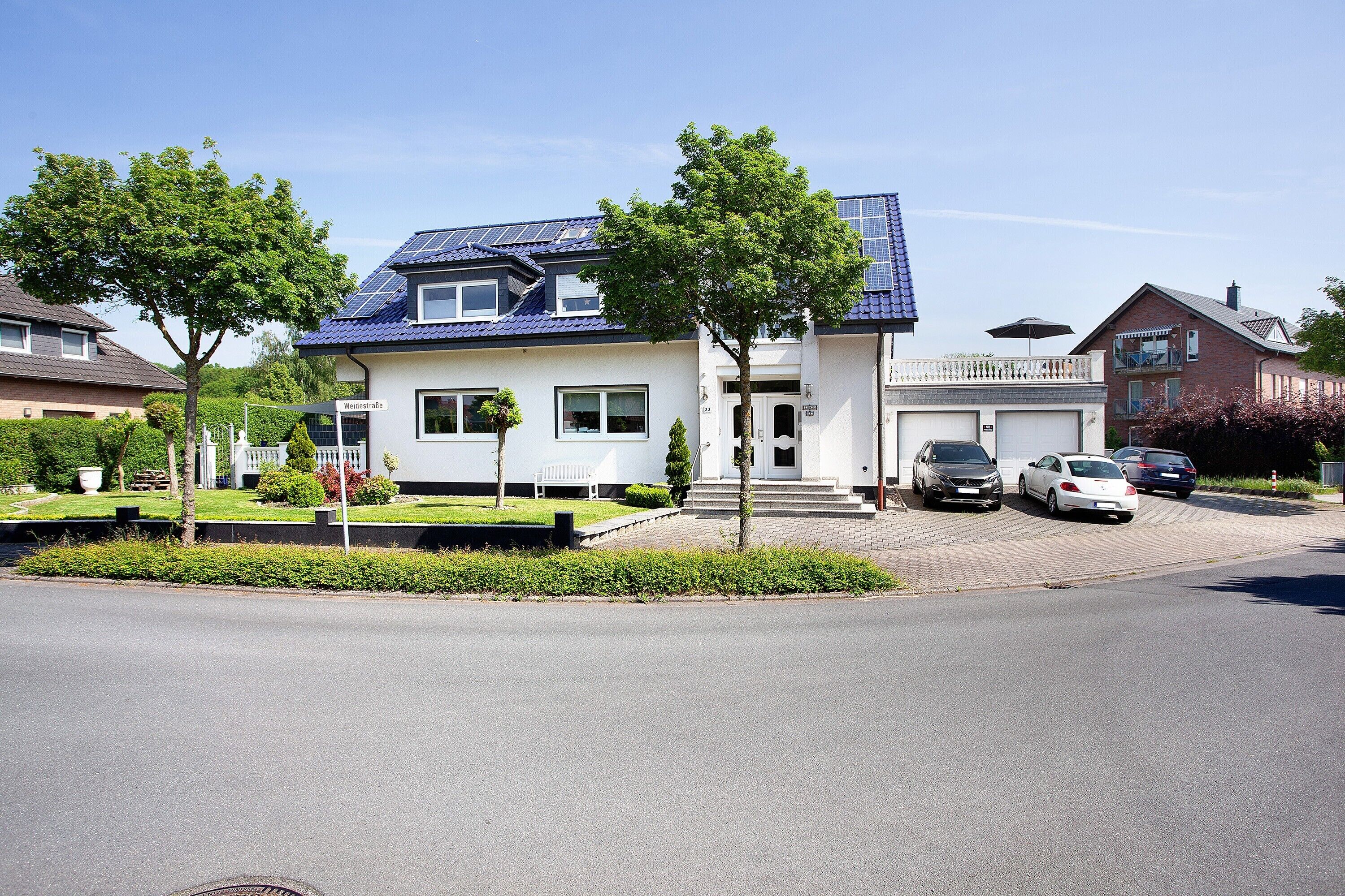 Een modern herenhuis met twee verdiepingen, een blauw dak, een garage en een oprit met geparkeerde auto's.